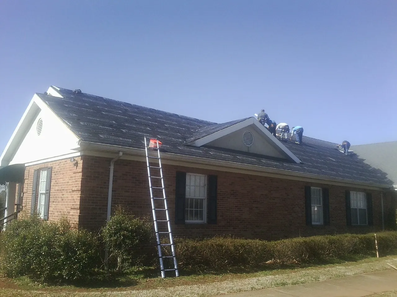 Crew tearing shingles off a brick ranch roof with a ladder set — Emergency Roof Repair work by our crew in Pewee Valley