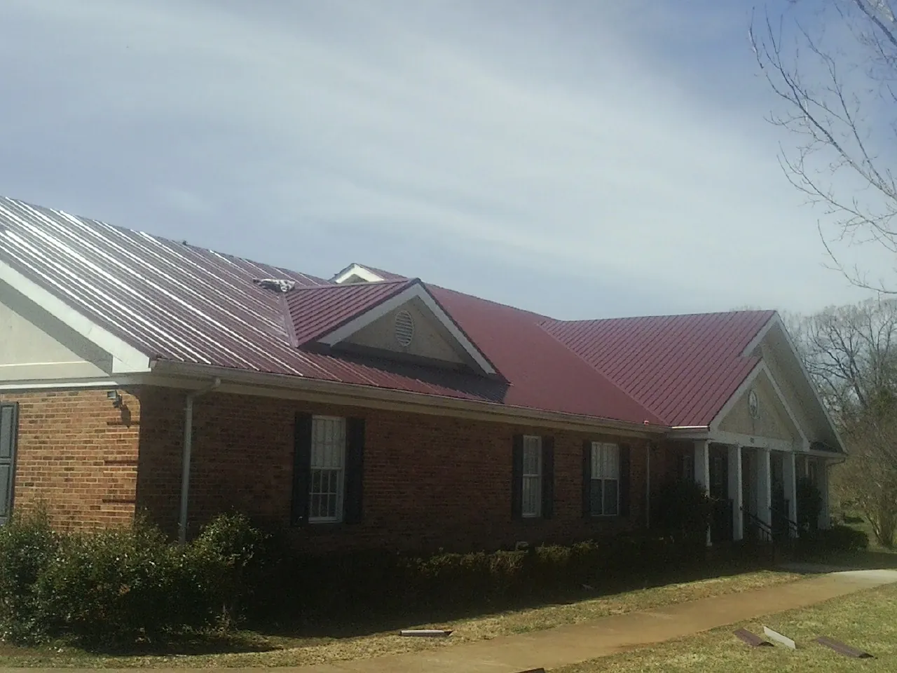 Red metal roof with gabled entries on a long brick building, from a Hail Damage Roof Repair job in Pewee Valley