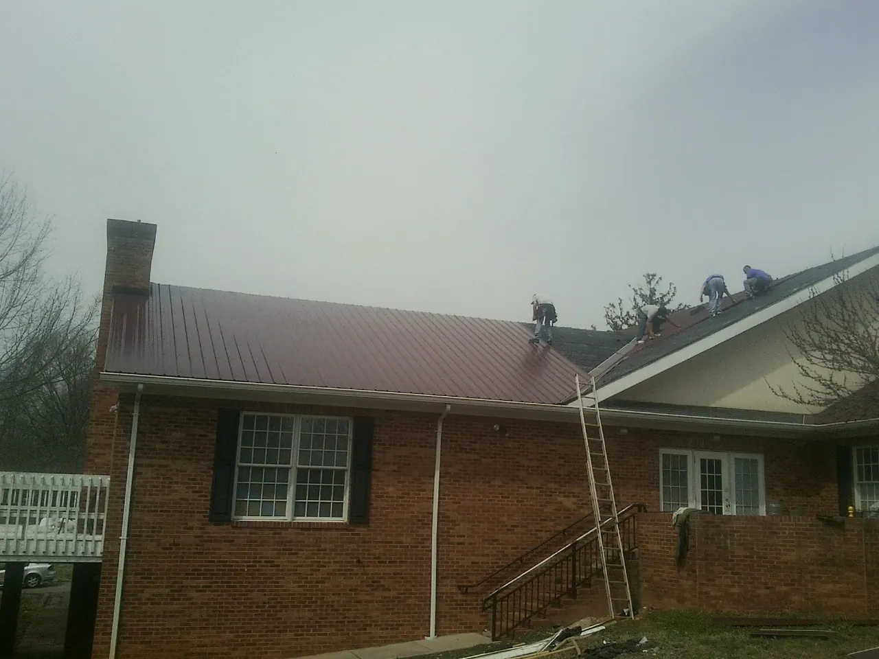 Crew setting red metal roofing panels on a brick home in Pewee Valley