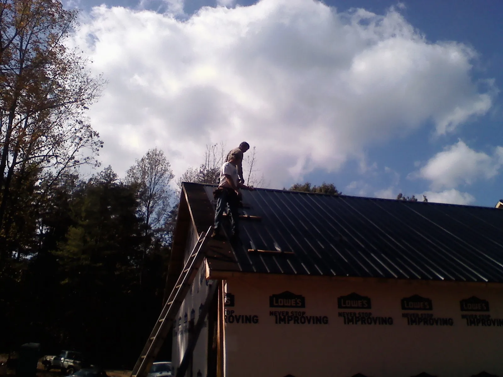 Roofer fastening dark metal panels high against a cloudy sky, from a Roof Inspection job in Pewee Valley