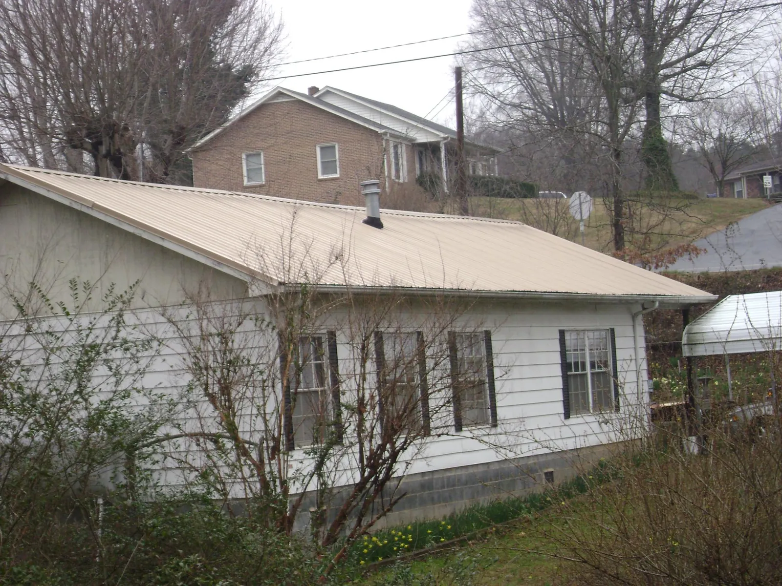 Tan metal roof on a white sided house set into a hillside — Commercial Roofing by Roofing Brothers in Pewee Valley